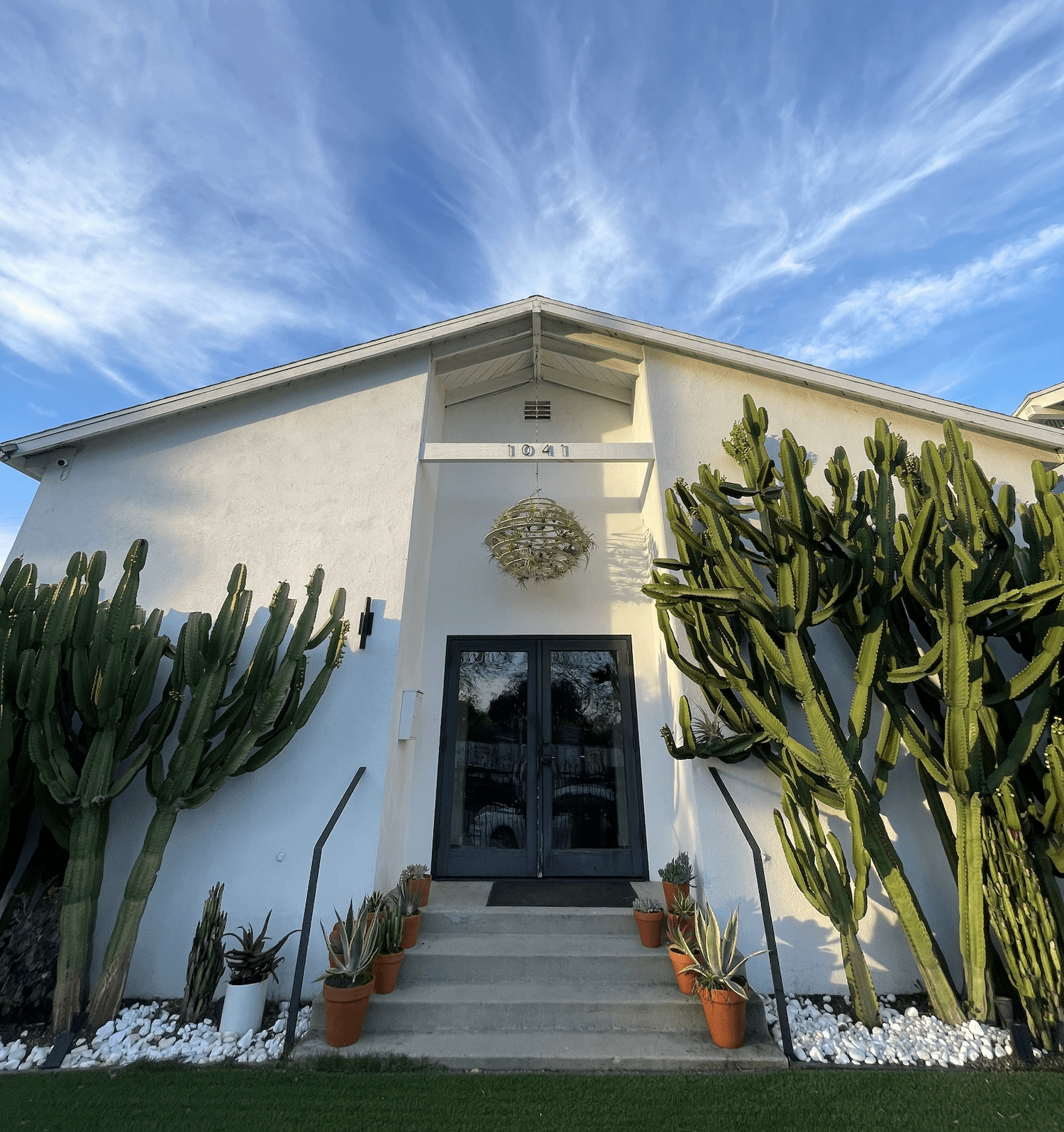 The white Abbot Kinney frontage of Reserve Venice, tall cacti and potted plants either side of the entrance